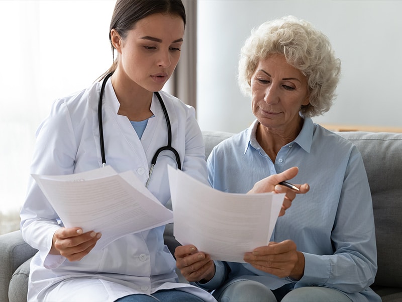 Young woman doctor visit senior old lady patient at home explain medical documents insurance, attentive female give consultation close sign healthcare agreement with elderly grandmother at home